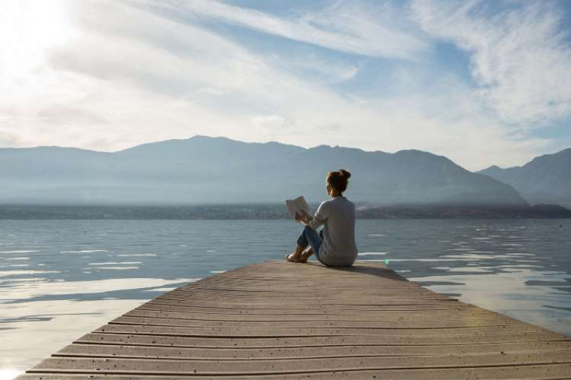 Girl sitting at the end of wooden pier reading a book