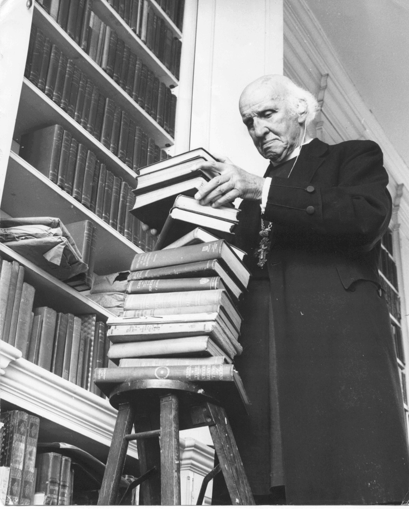 Photograph of Hewlett Johnson with a large pile of books, likely in the Deanery.
