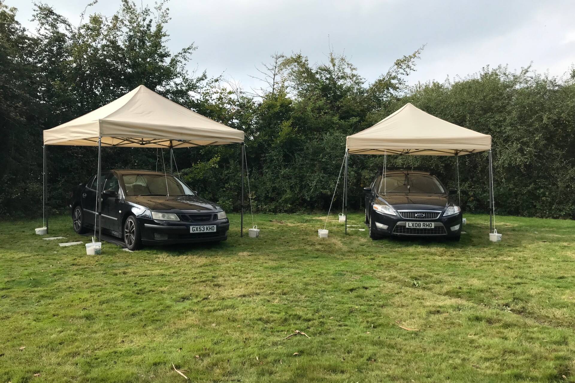 Two cars in a garden with tents over them