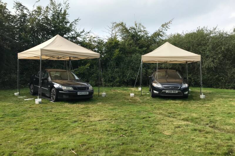 Two cars in a garden with tents over them