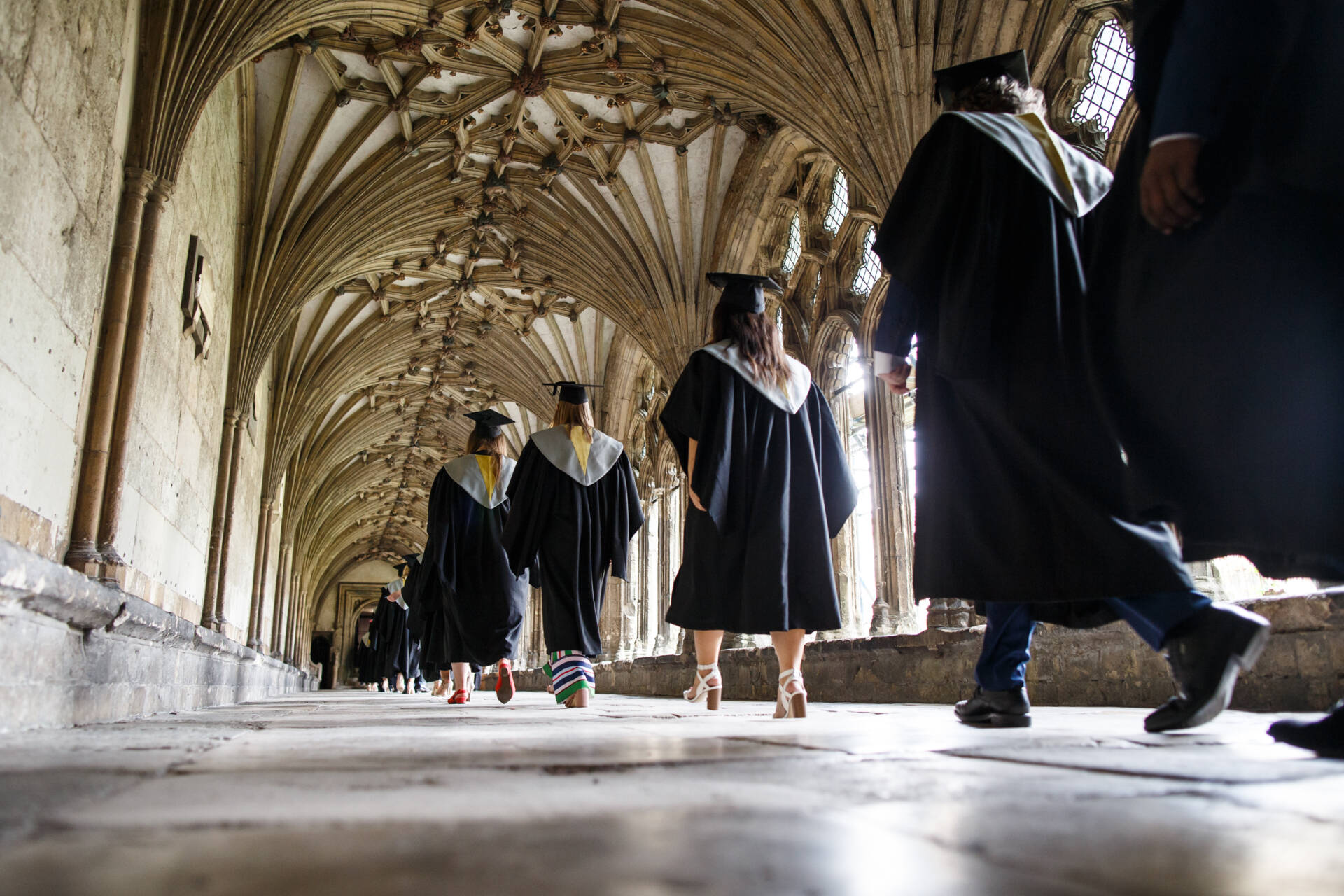 Students wearing graduation cap and gowns walking in the Cloisters at Canterbury Cathedral