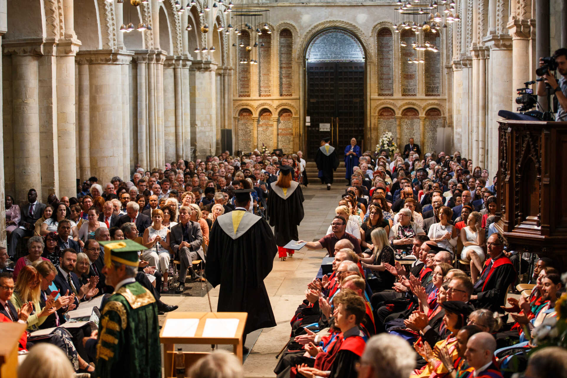 Students wearing graduation caps and gown process down the central aisle of Rochester Cathedral on graduation day