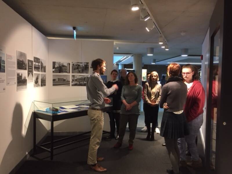 Staff member talking to a group of people in the gallery space, with wall mounted images and a display case