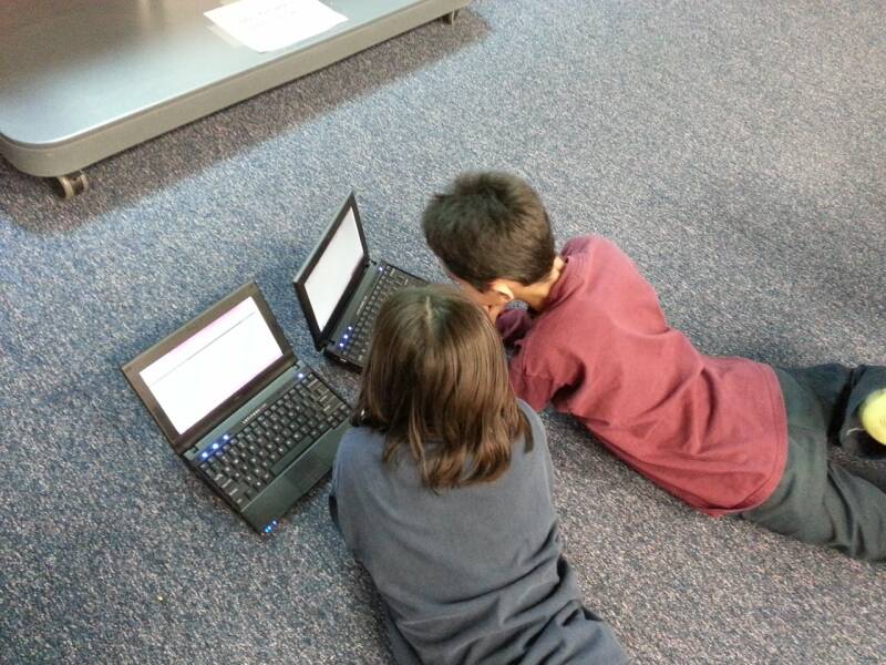 Two children on the floor looking at laptops