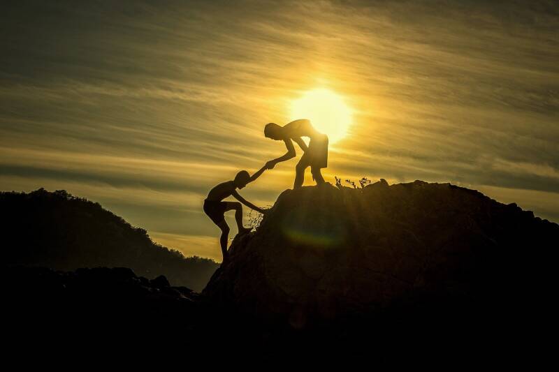 Some one helping another person climb up a cliff