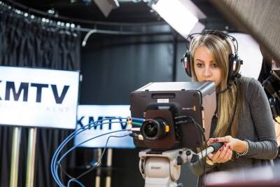 Student wearing headphones and using a television camera in a KMTV studio