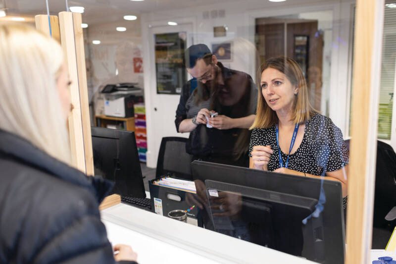 A smiling woman behind a counter, talking to a student