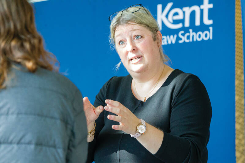 A woman talking to a student, standing in front of a Kent Law School sign