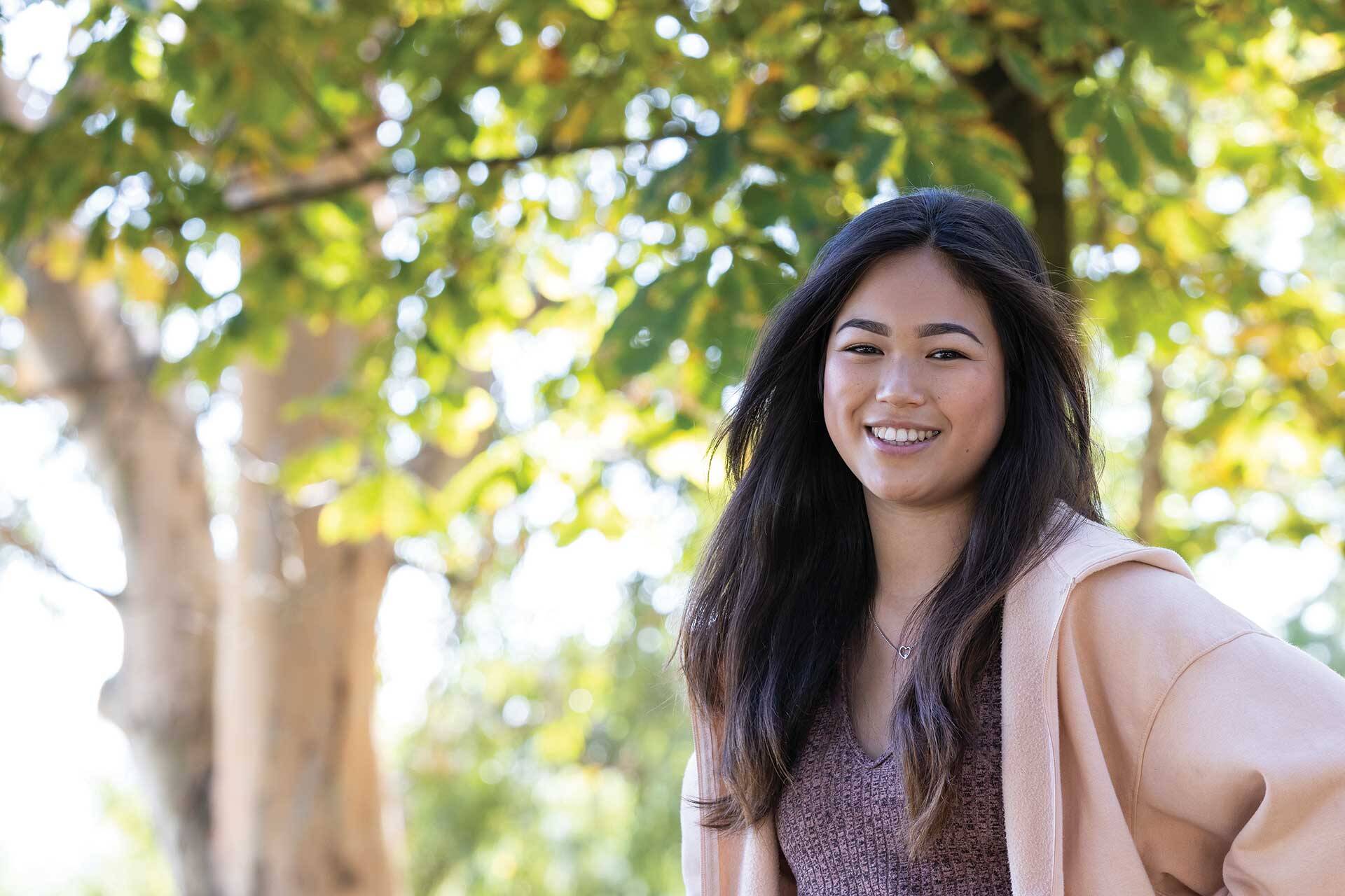 Young woman smiling, with trees in the background.