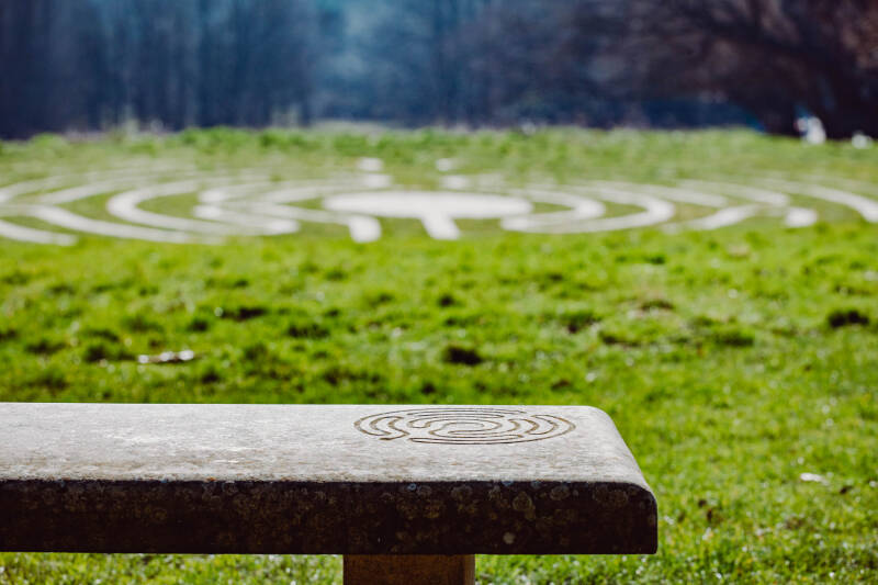 A bench, and the labyrinth on the floor in the background, with trees.