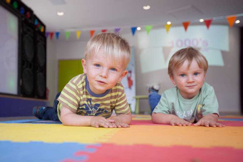 Two toddlers on a mat look at camera