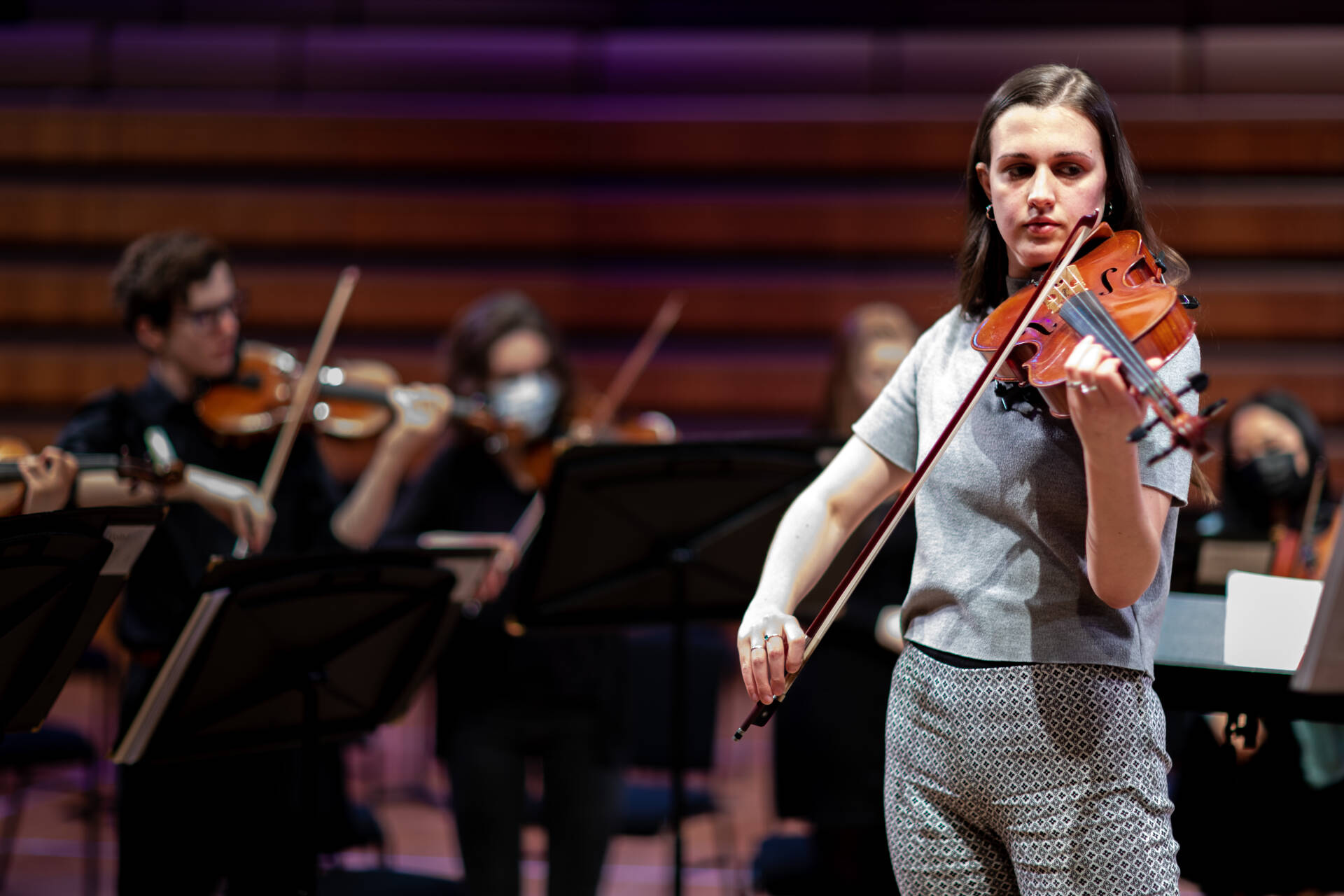 Female viola player dressed in grey, behind her out of focus other string players wearing black