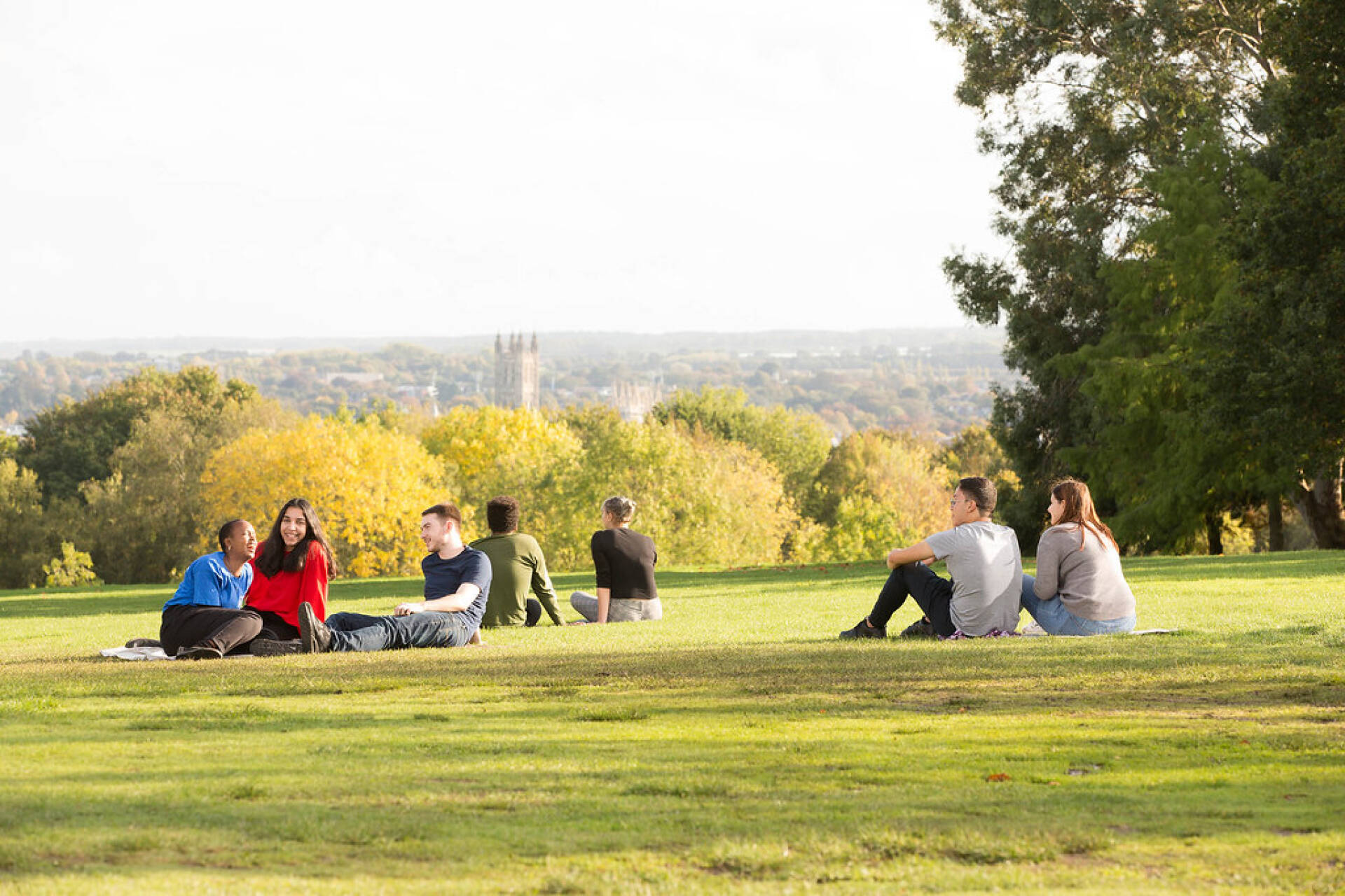 People sitting on the grass, with a view overlooking Canterbury Cathedral.