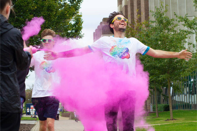 Man running towards the camera while pink paint powder is thrown at him during Colour Run