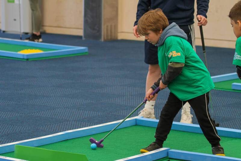 Child in green t-shirt playing mini golf, about to hit the ball
