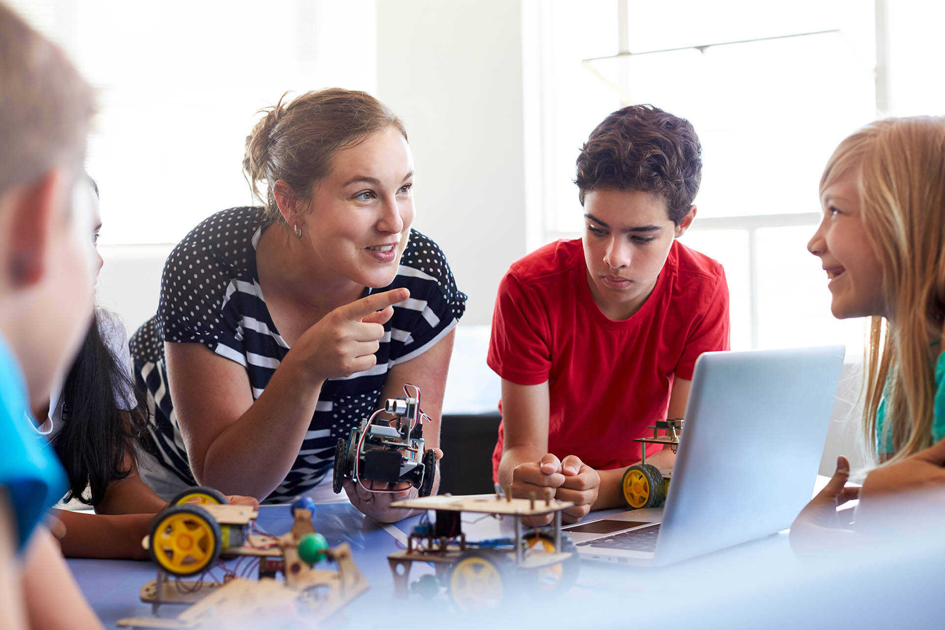 Teacher engages with group of school students building vehicles in a classroom