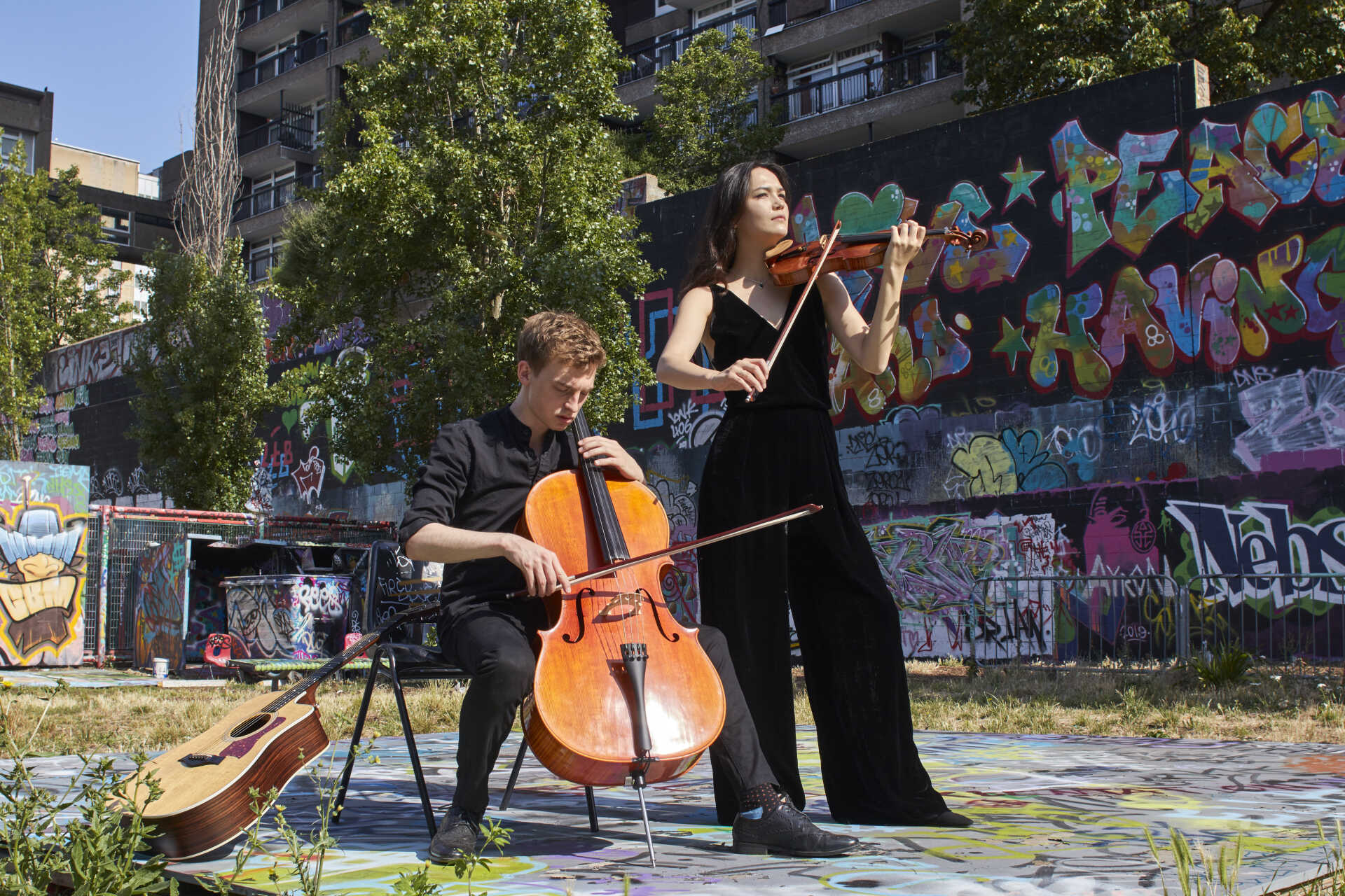 Seated cellist and standing violinist against an urban background of a graffiti-strewn wall