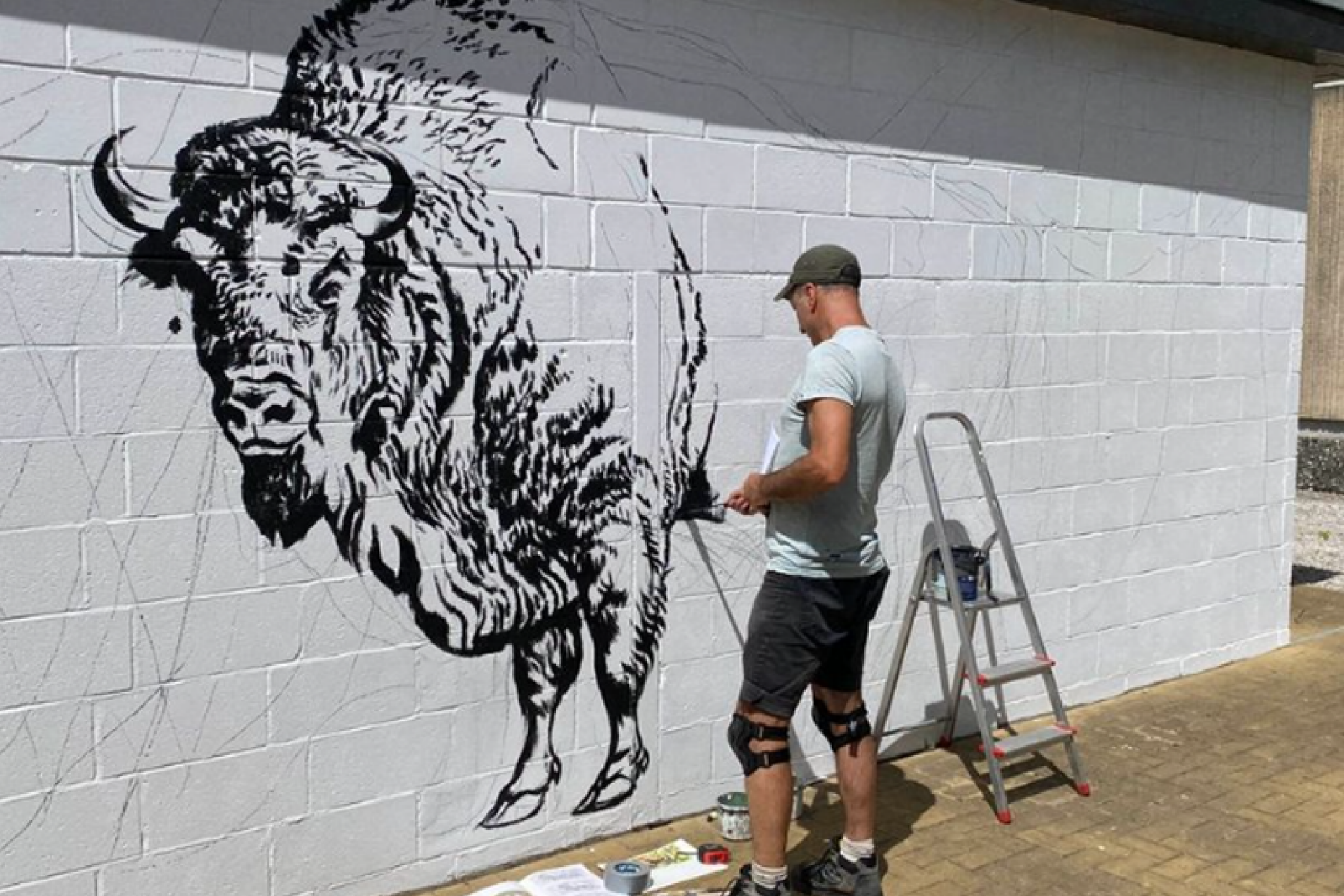 A man painting a Bison mural onto a brick wall.