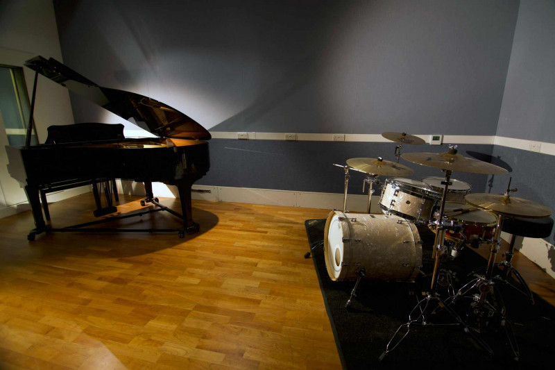 Studio with a wooden floor and grey walls, containing a grand piano and a drum kit