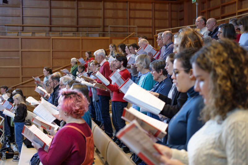 Side photo of a large group of singers in tiered rows in a rehearsal