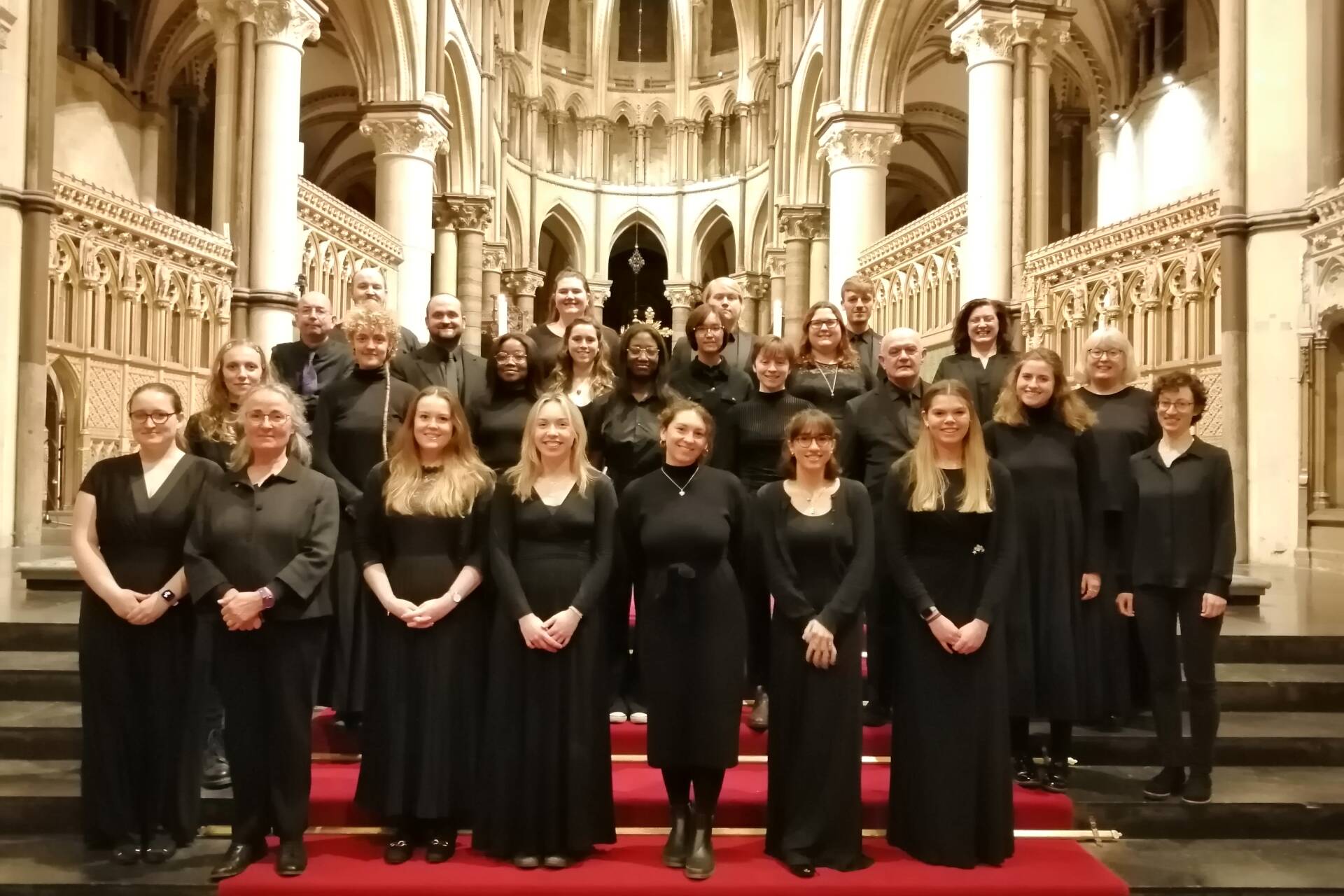 Choir standing on red-carpeted steps wearing formal black in Canterbury Cathedral