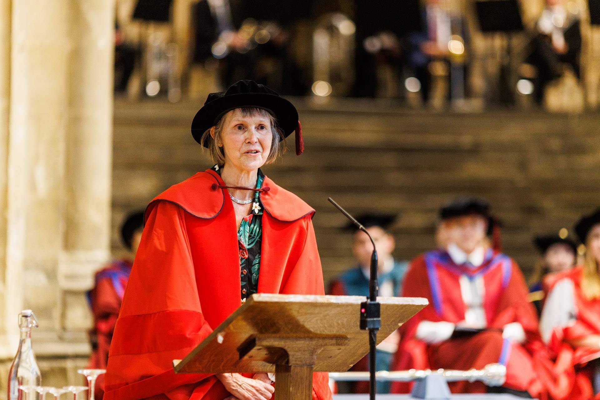 Susan Wanless speaking in Canterbury Cathedral at her honorary degree conferral, wearing red robes and a tudor bonnet