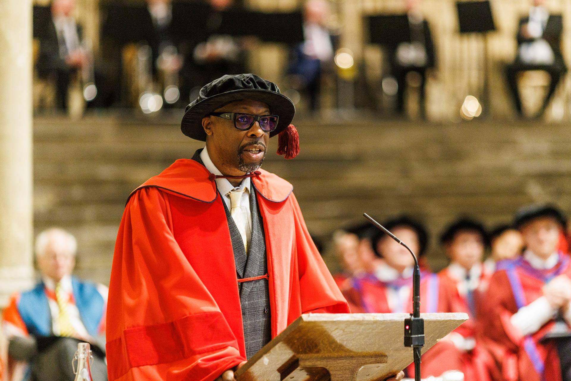 Professor Kevin Hylton  speaking in Canterbury Cathedral, wearing red robes and a tudor bonnet