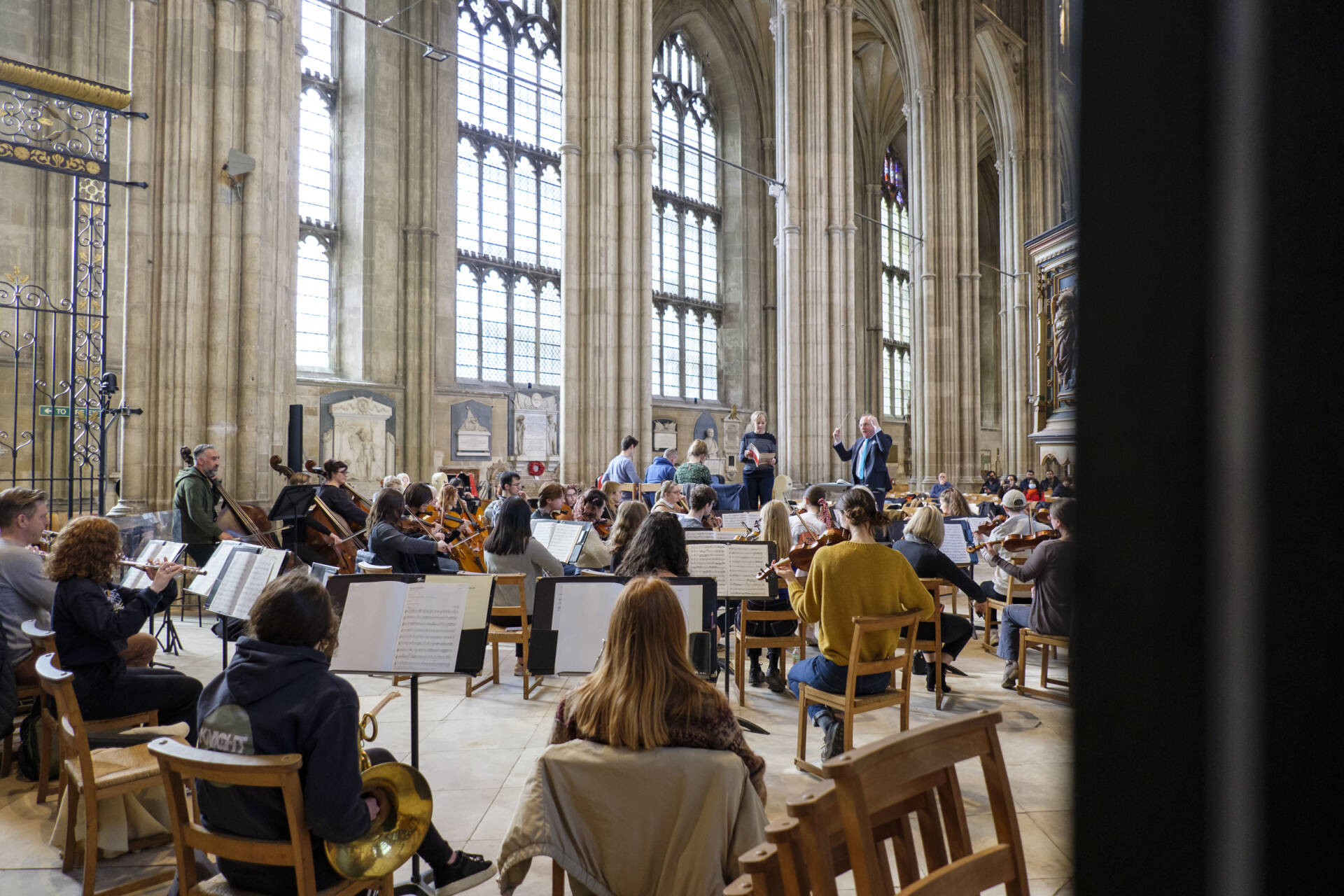 View from behind a group of orchestral players rehearsing in the Nave of a cathedral