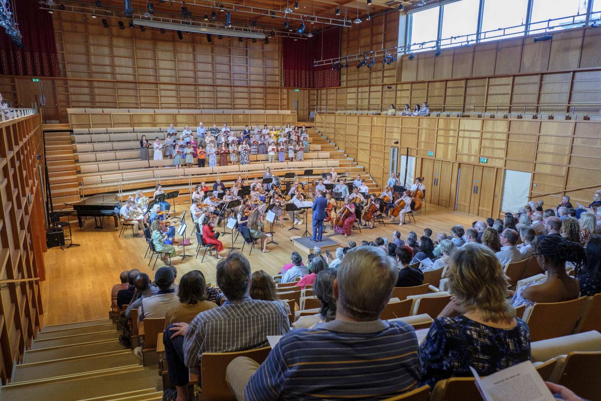 Group of orchestral players and a choir performing in a concert-hall, view from behind the audience