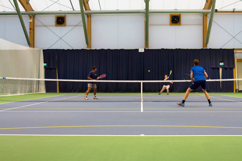 A group of students and staff playing tennis on the indoor courts.