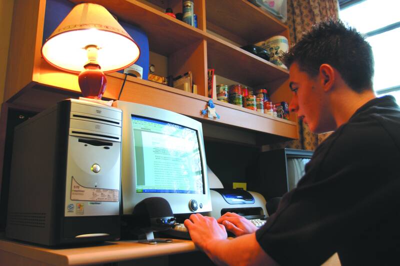 Colour photograph of male student in study bedroom with an old fashioned computer.