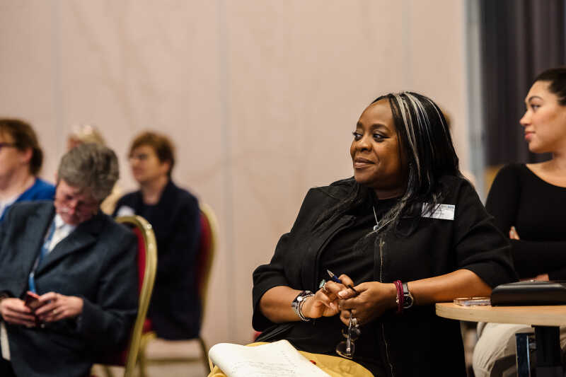 A woman dressed all in black watching a speaker at a conference