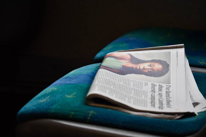 The edge of a tube train seat and a newspaper with a photo of a young black woman. with a headline about racist abuse.