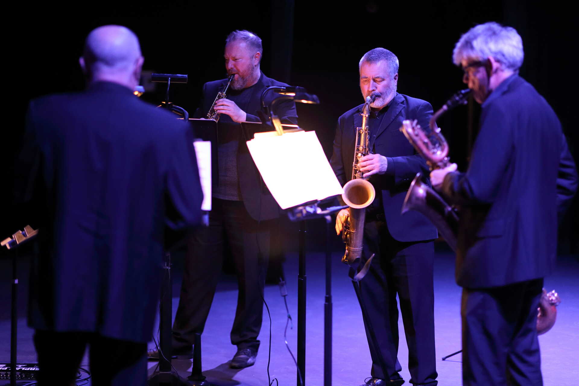 Four male saxophonists performing beneath purple lighting