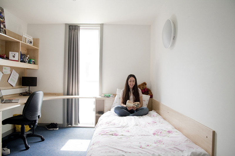 Female student sitting on her bed reading a book.
