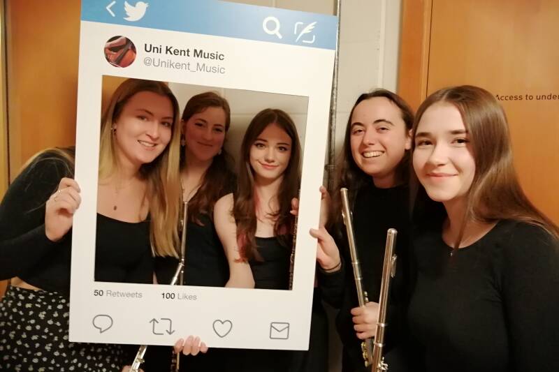 Five female flute players; three managed to get behind the selfie frame, two didn't...