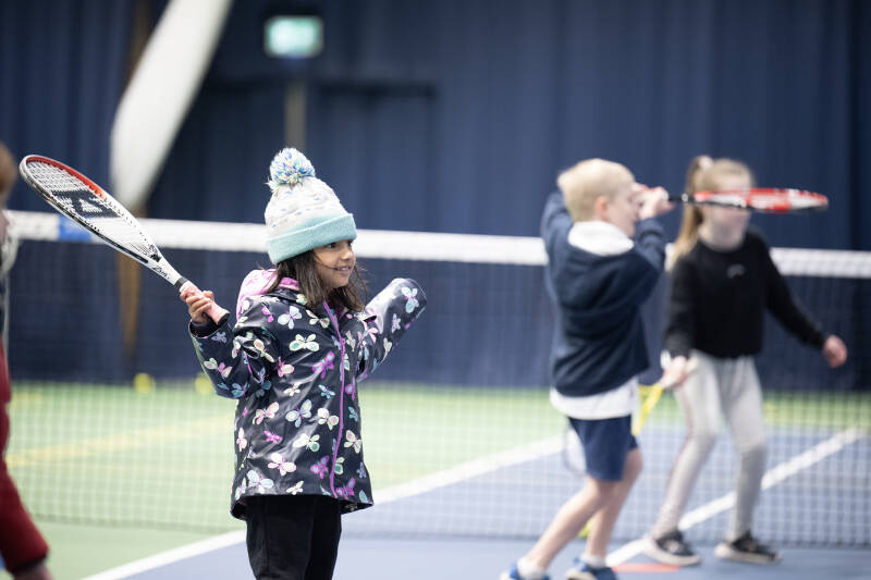 Young children smiling as they play a game of tennis as a group.