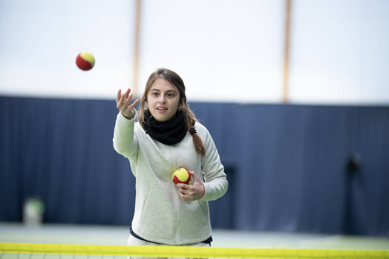 Woman throwing tennis balls over the net during a tennis coaching session