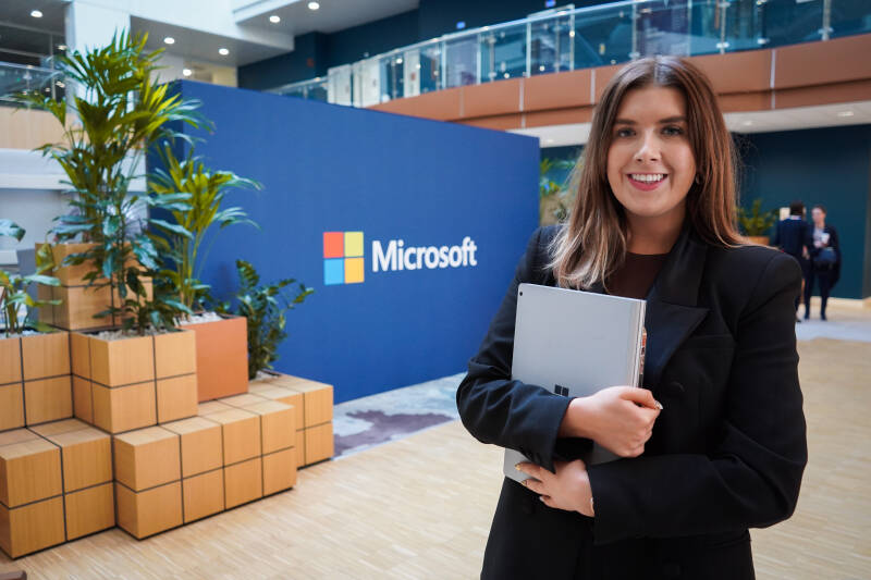 Image of KBS alumna, standing in front of Microsoft sign. She is smiling and holding a laptop.
