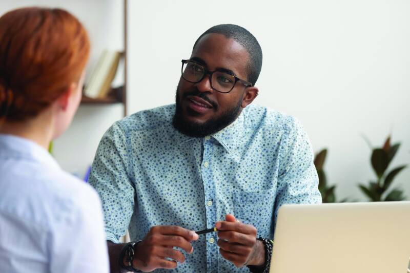 Photo of young man in conversation with someone in an informal office setting.