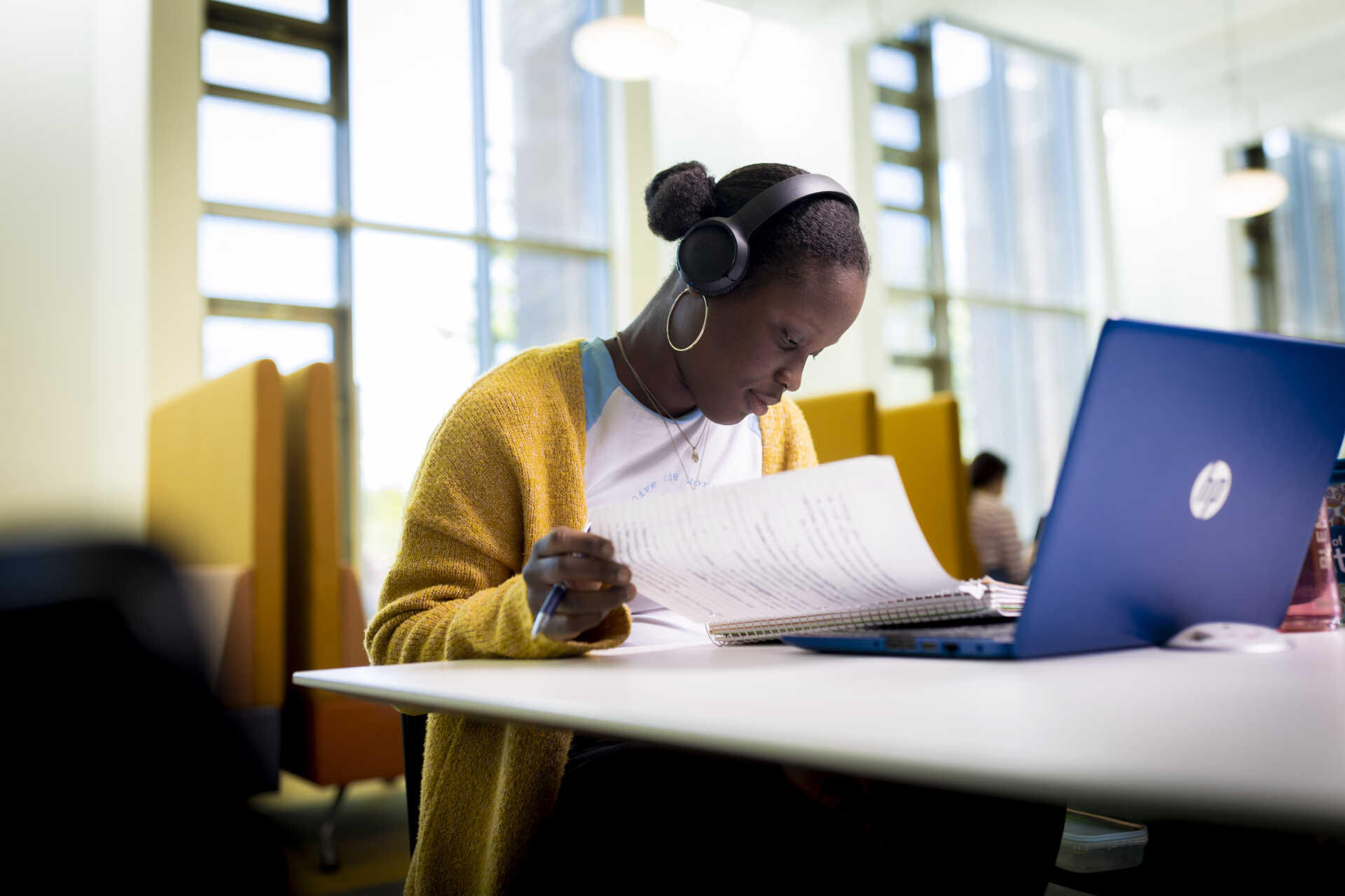 Student with headphones on looking at notes next to laptop