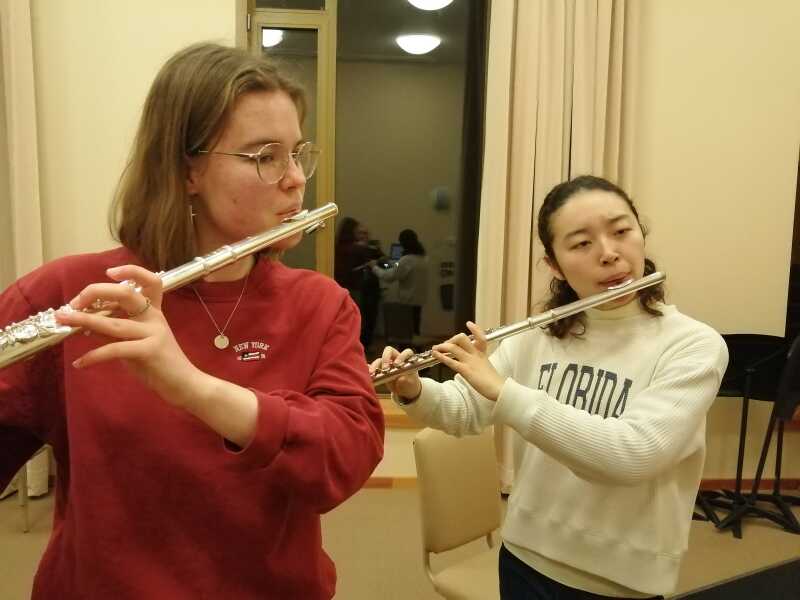 Two female flute players playing in a rehearsal room