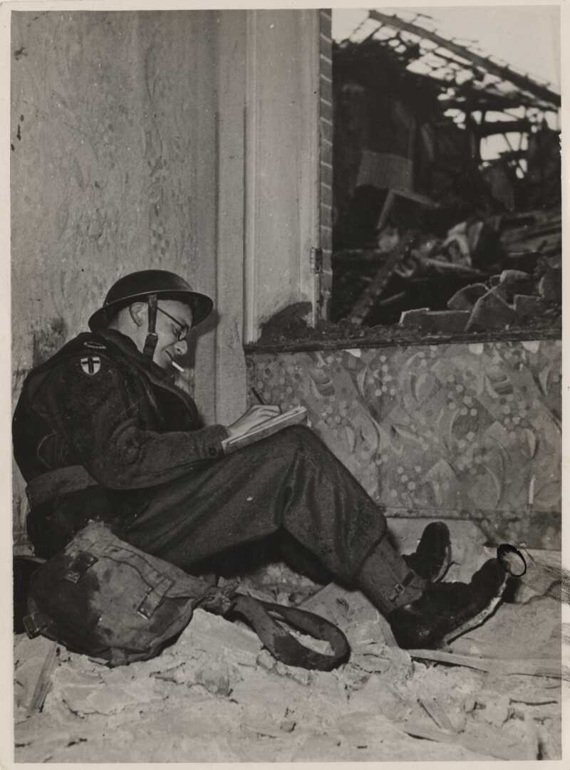 A black and white photo of Giles sitting and sketching in war damaged building