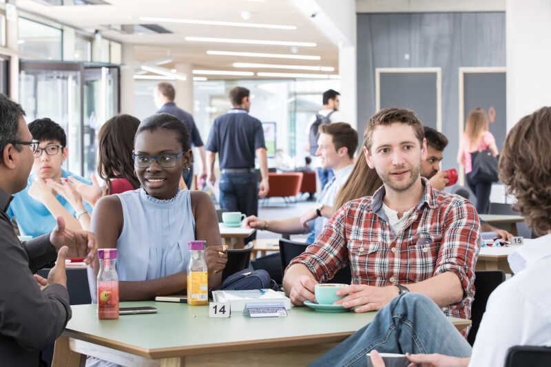 A group of students sat around a table enjoying conversation and hot drinks