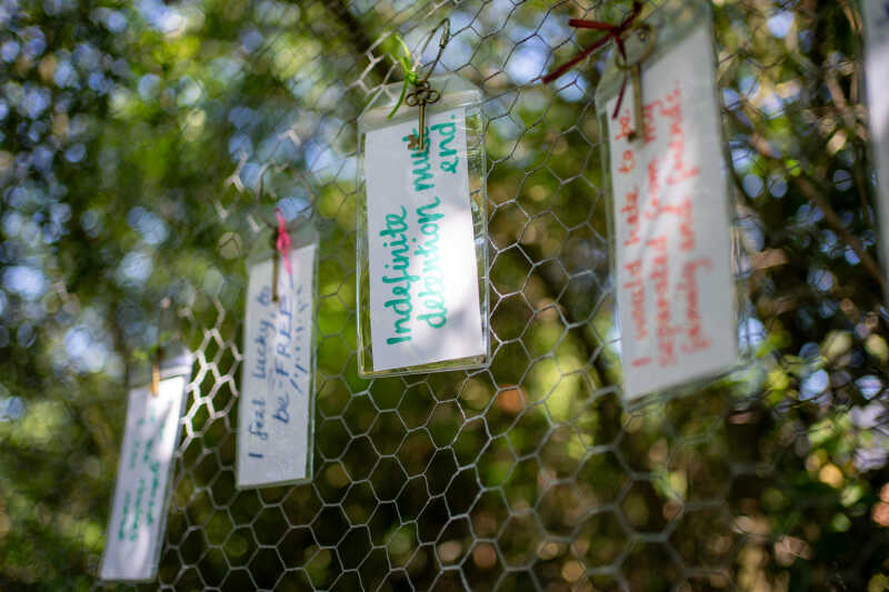 Luggage tags with messages in coloured pen attached to wire fencing on backdrop of greenery