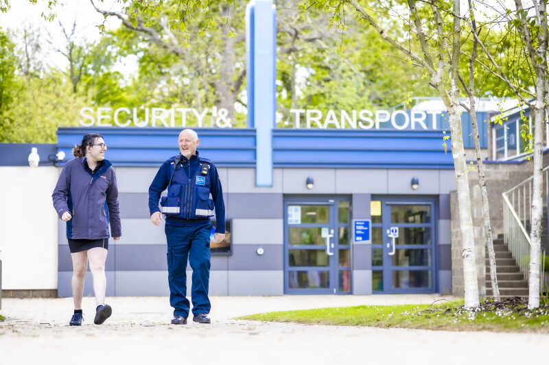 Security officer and student walking together in front of Security and Transport Centre.