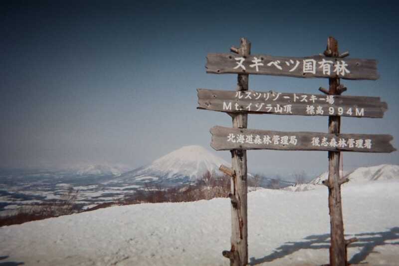 Wooden signpost on snow-covered Mount Isola with view of Mount Yotei volcano in the distance