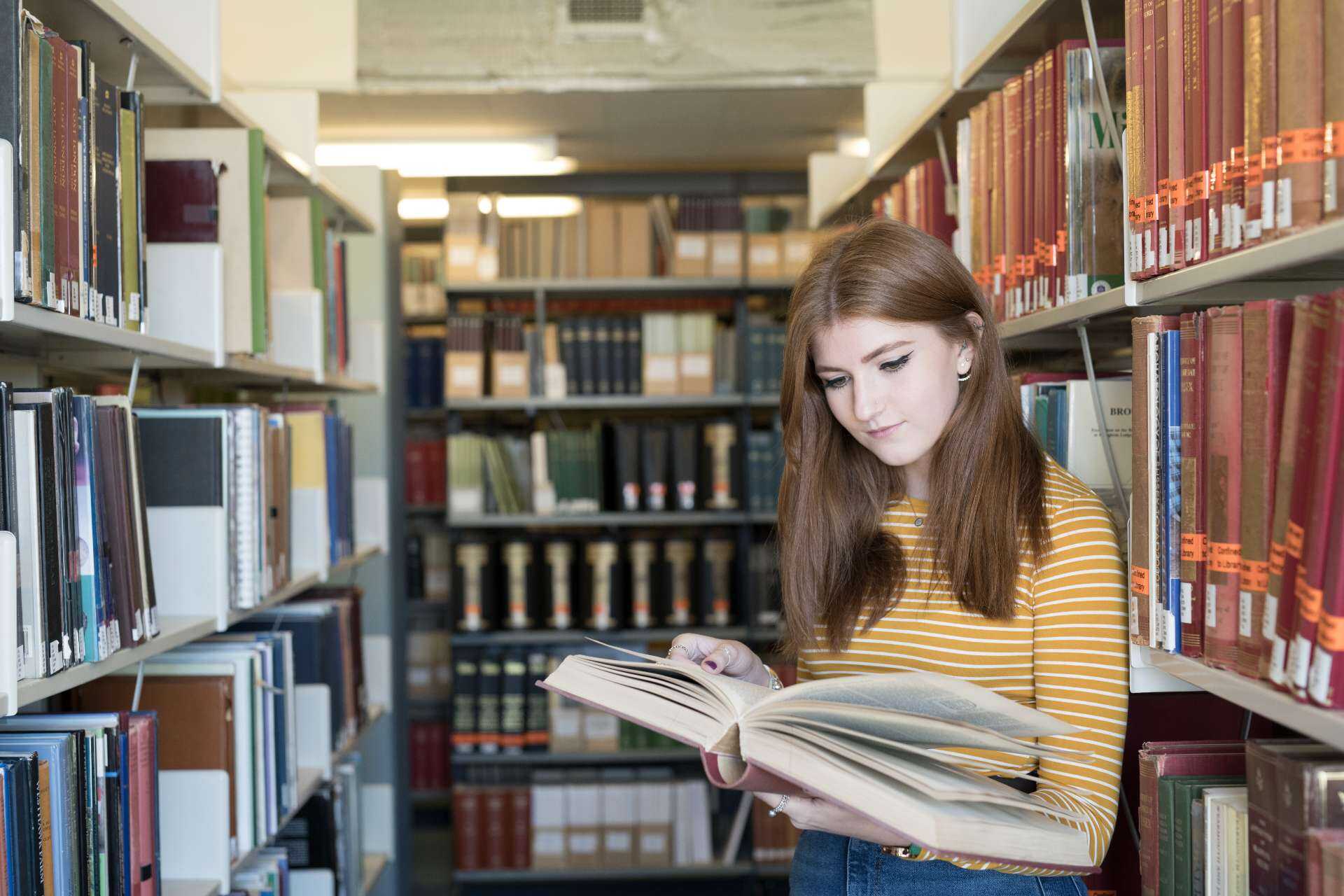 Photograph of female University of Kent student in University library, looking through an open book