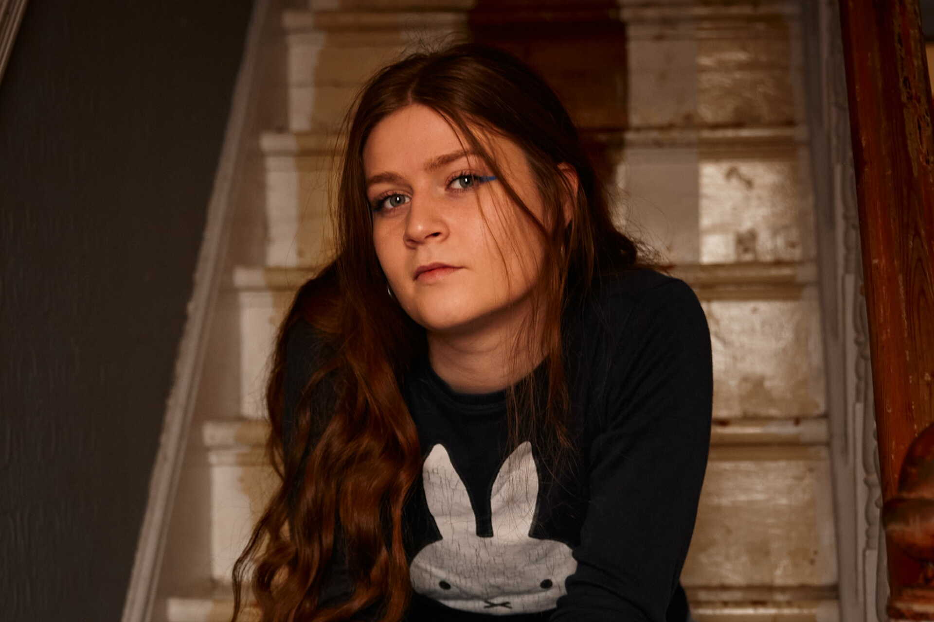 Young woman seated on a staircase gazes reflectively at the camera