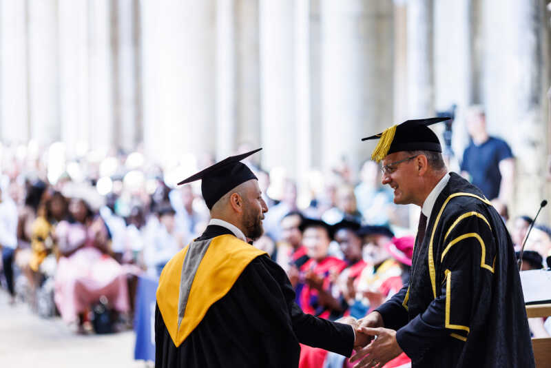 A masters student is shaking the hand of the vice-chancellor at their graduation